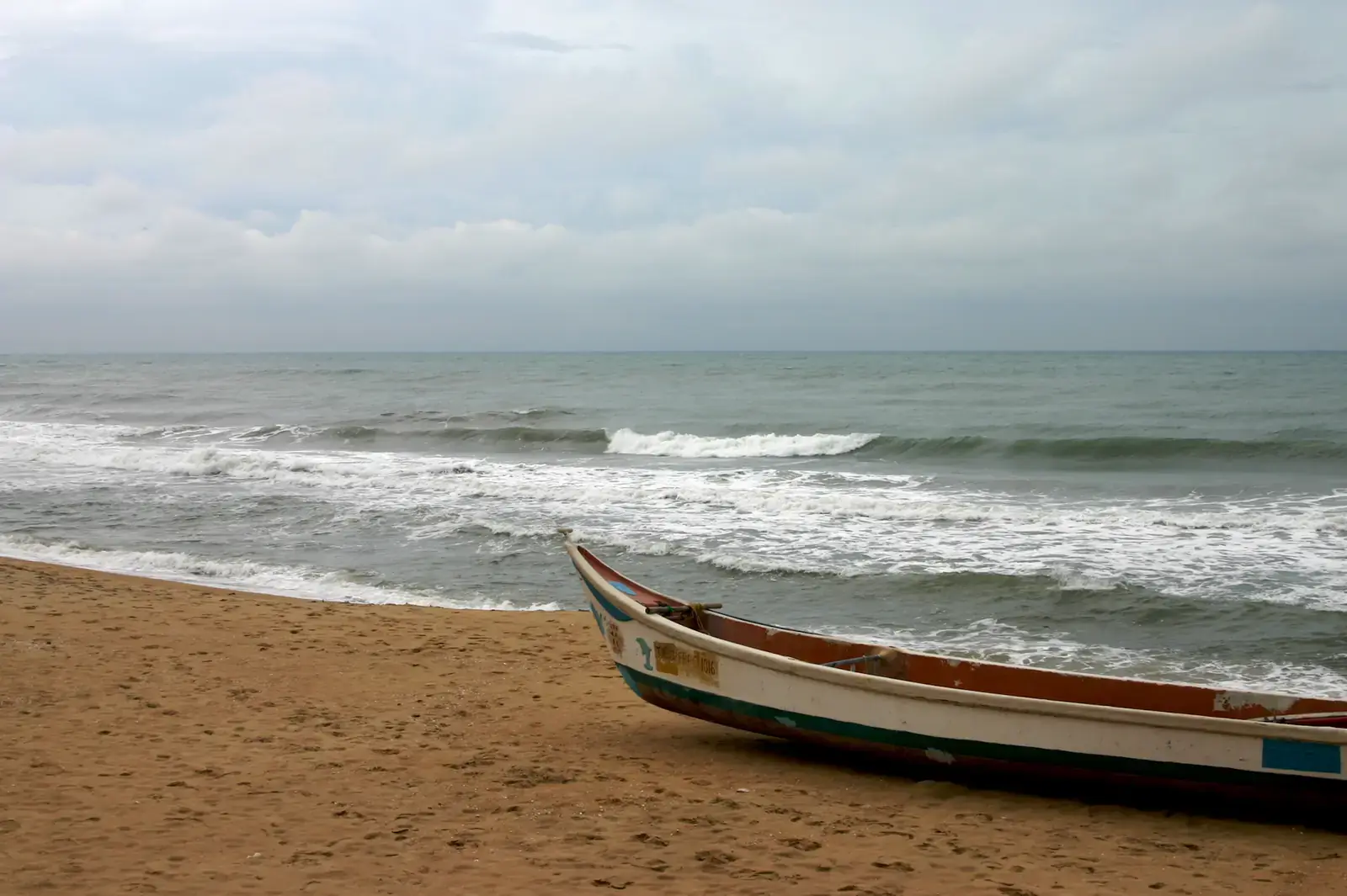 Waves breaking on Covelong beach near Chennai, with a fishing boat on the sand