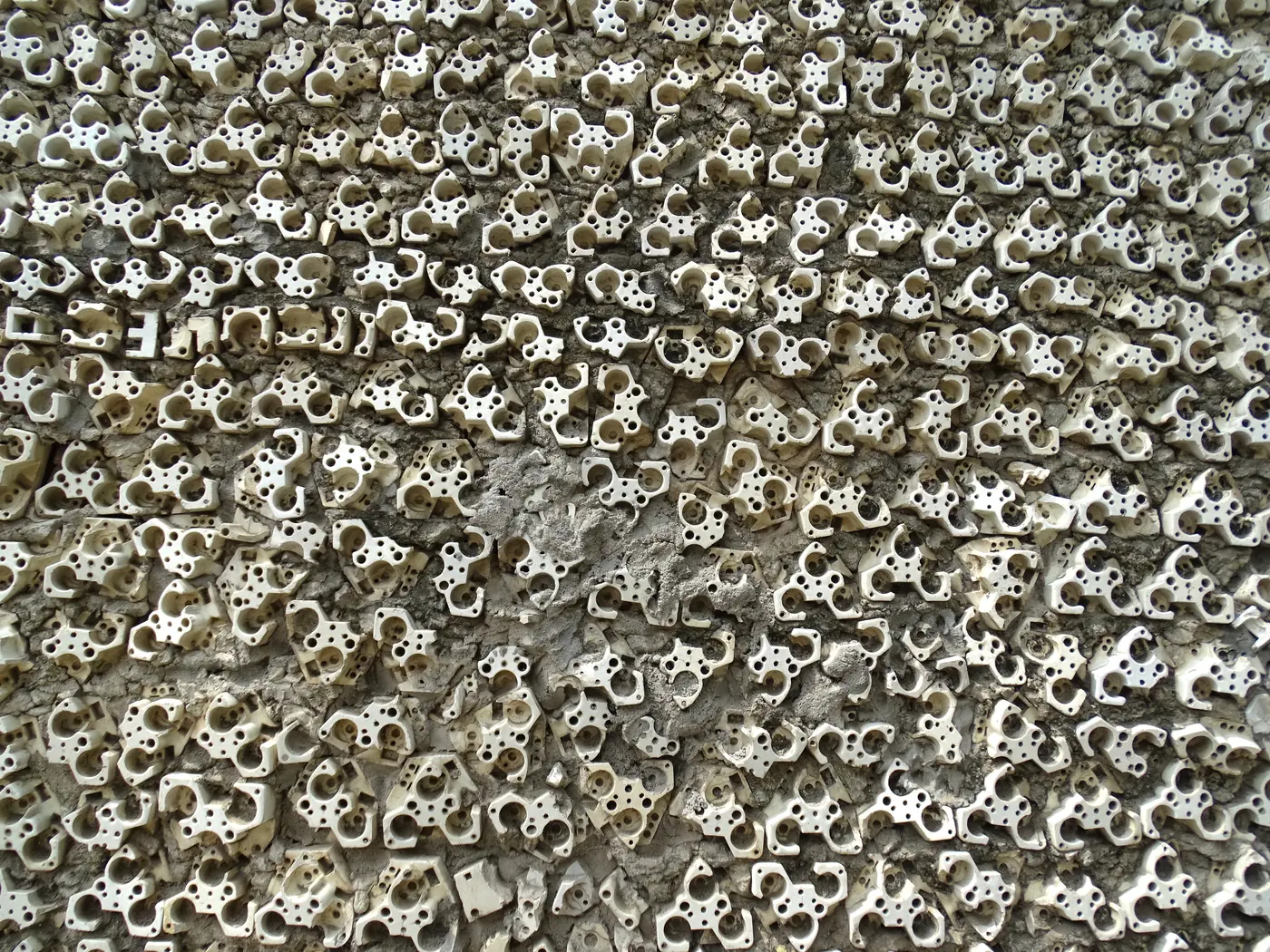 Close-up of a Rock Garden wall densely studded with discarded ceramic electrical fittings, showing the salvaged-material technique behind the sculptures