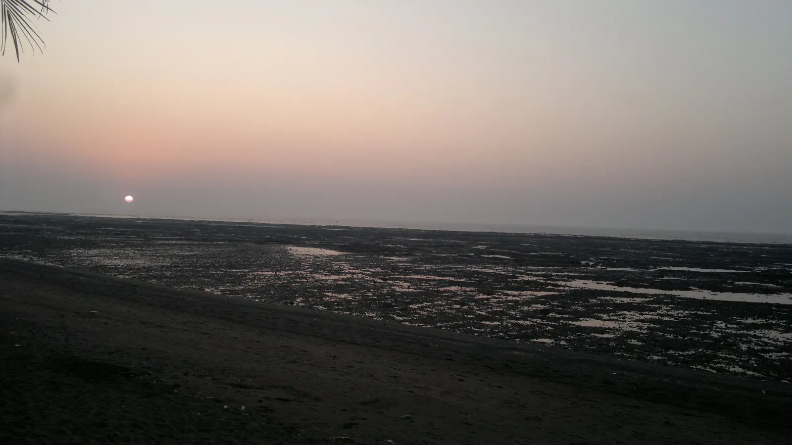 Sunset over the tidal flats at Devka Beach, sun dipping toward the Arabian Sea, Daman