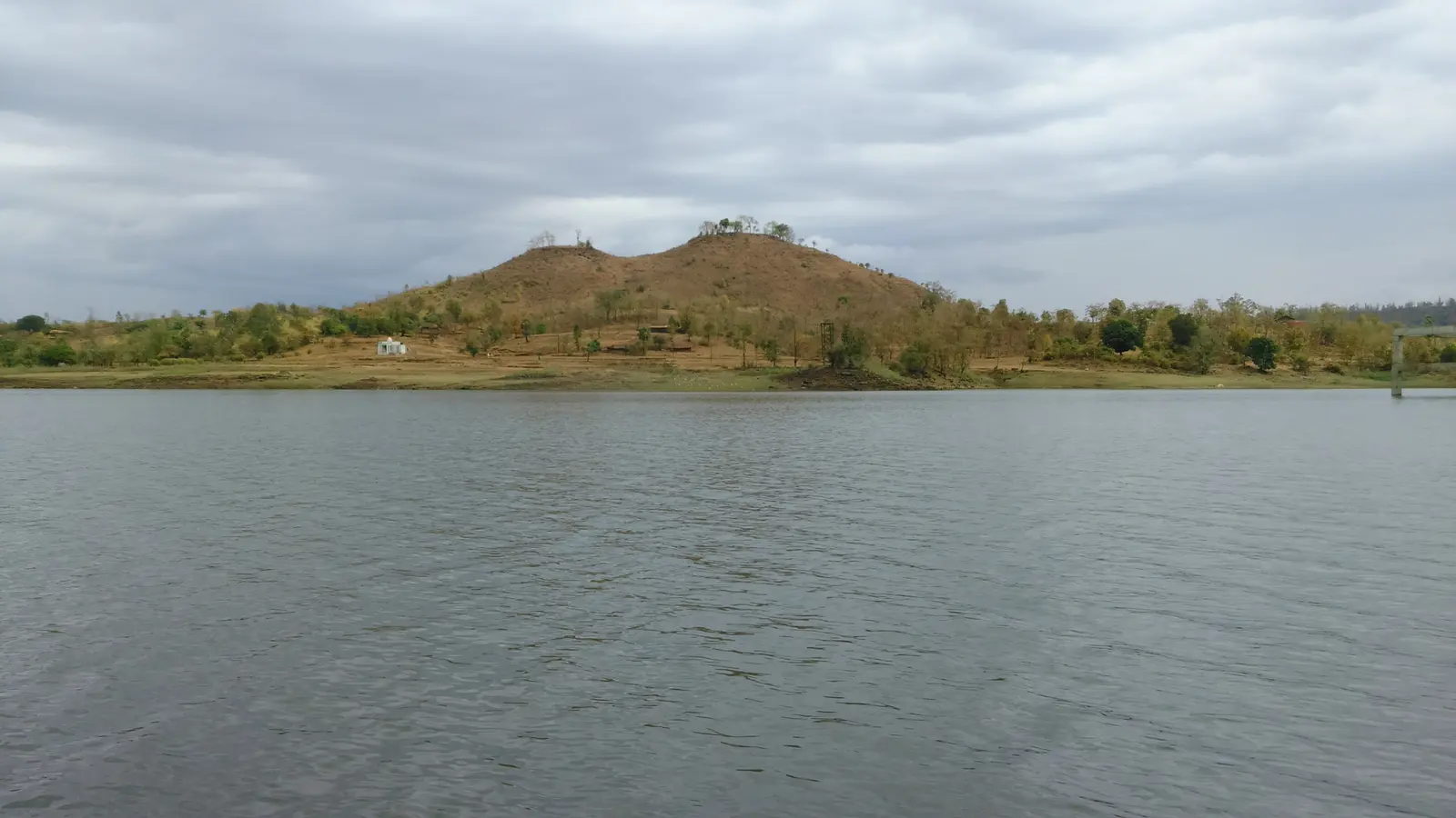 A forested hillock rising from the water of the Dudhni reservoir, seen from a boat on Madhuban Dam