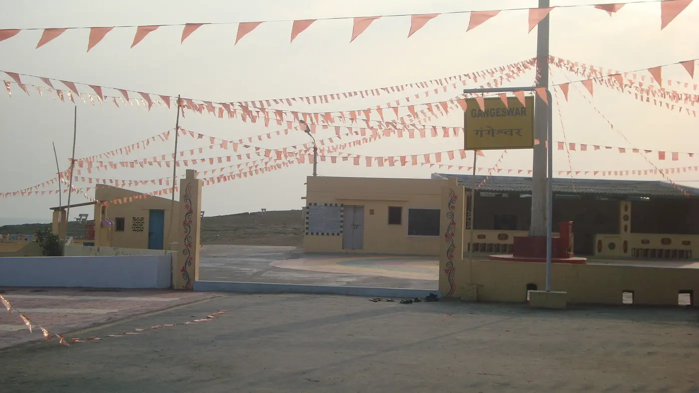 The Gangeshwar Temple entrance gate near Fudam, Diu, strung with saffron prayer flags, with visitors' footwear left at the threshold