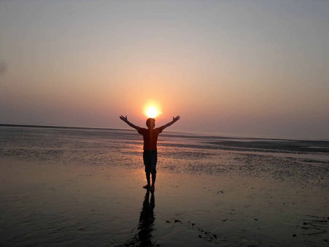 A visitor silhouetted against the setting sun on the wet, low-tide sand at Jampore Beach, Daman