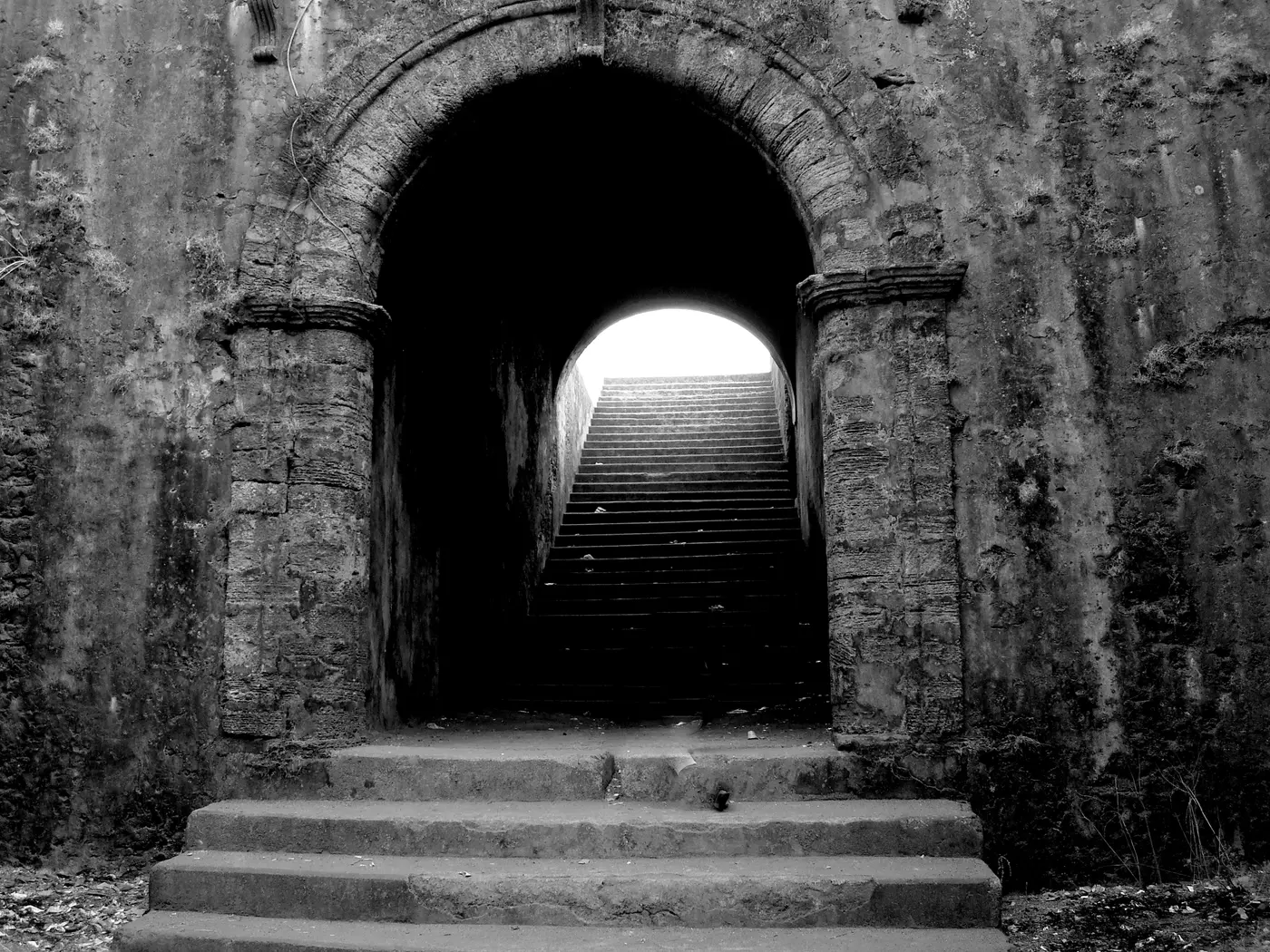 Worn stone steps rising through a vaulted archway inside Moti Daman Fort's ramparts