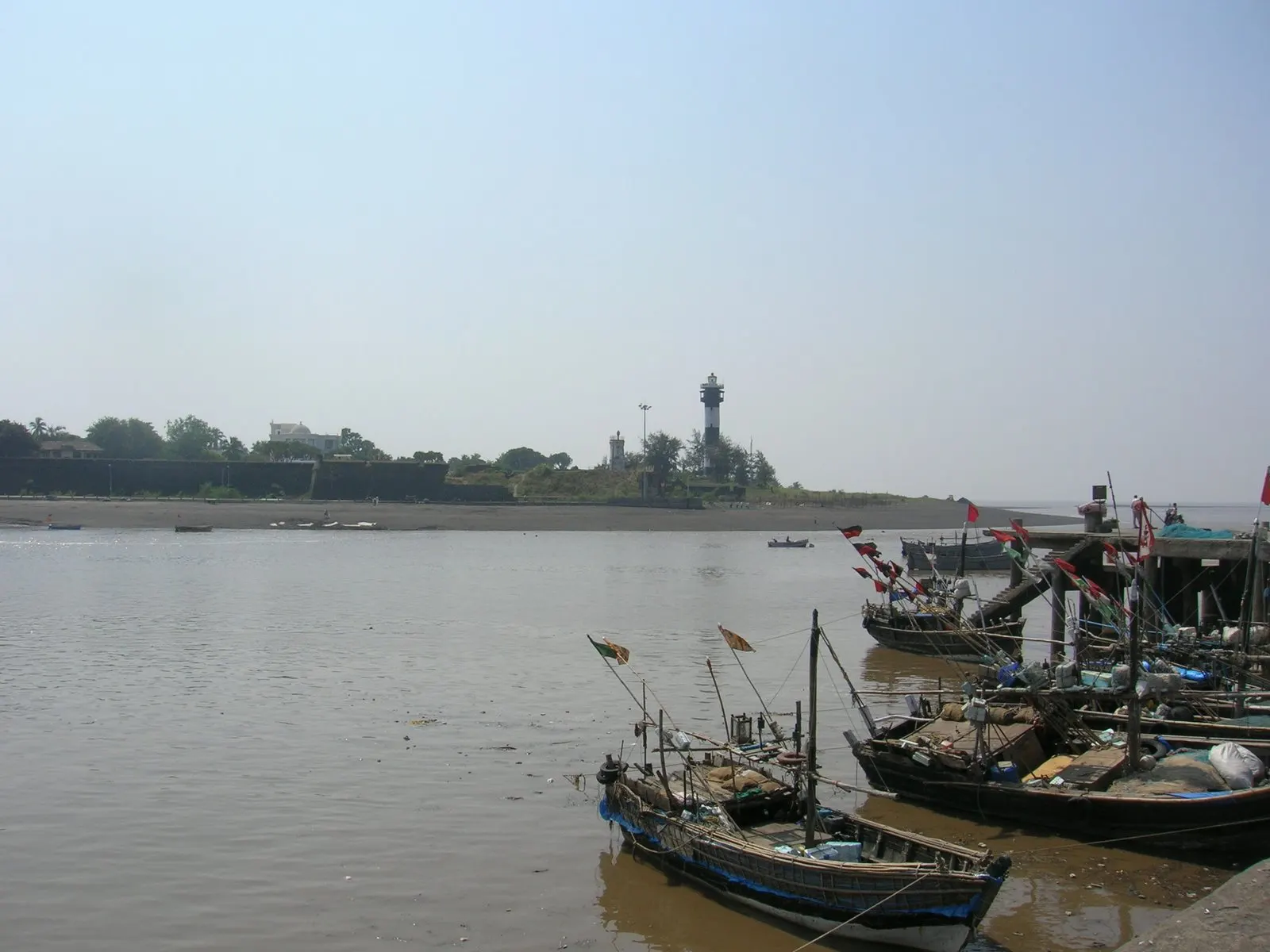 Fishing boats moored at Daman's harbour, with the fort and lighthouse visible across the water