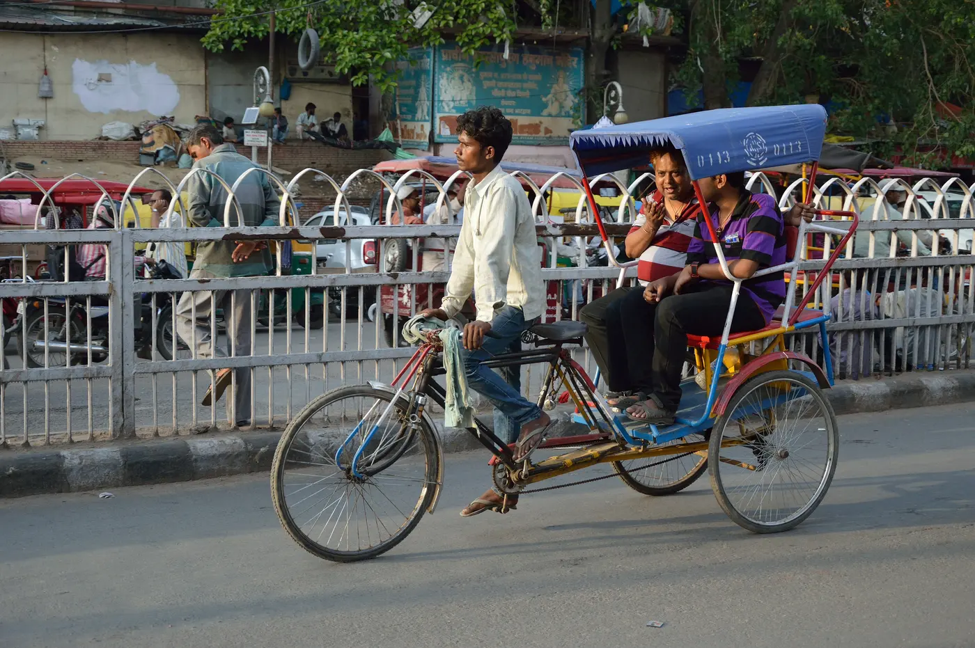 A cycle-rickshaw carrying passengers along a busy road near Chandni Chowk, Old Delhi
