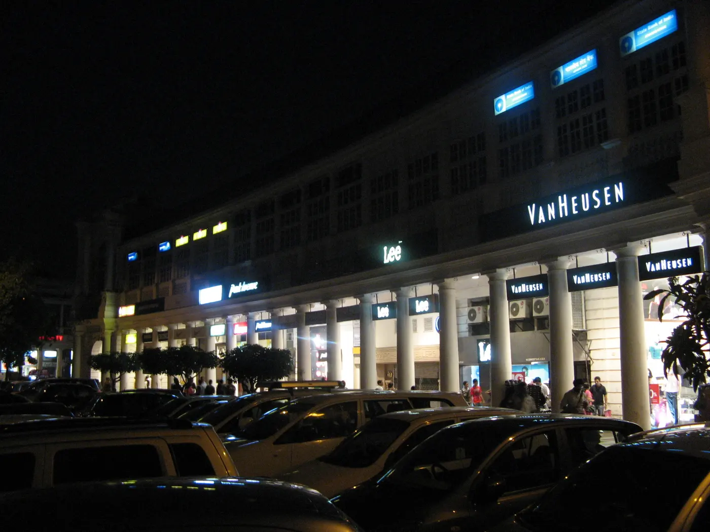 Connaught Place's colonnaded shopfronts lit up after dark, with branded stores beneath the arcade