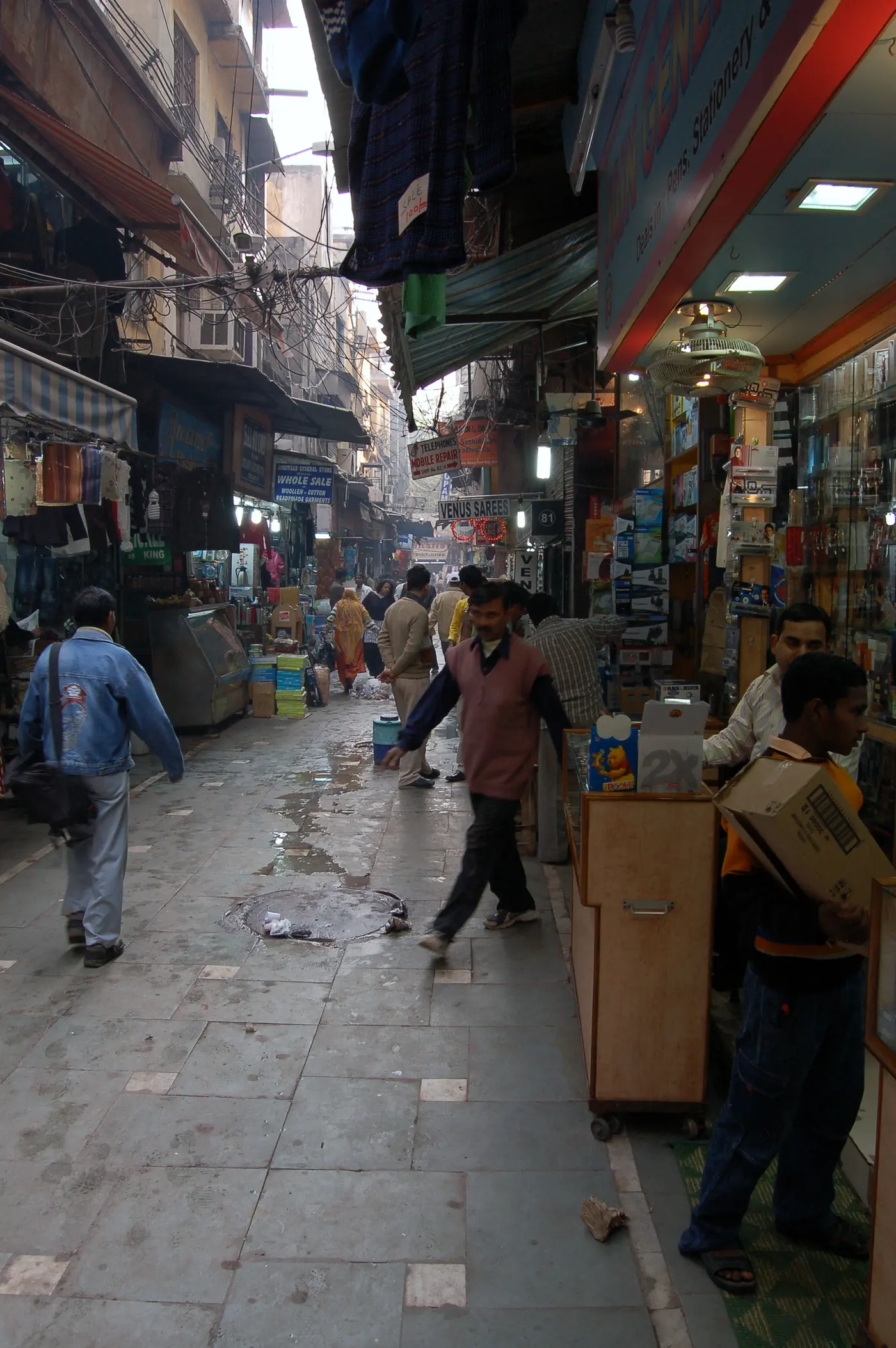 A narrow pedestrian lane inside Gaffar Market lined with mobile repair and electronics stalls, Karol Bagh