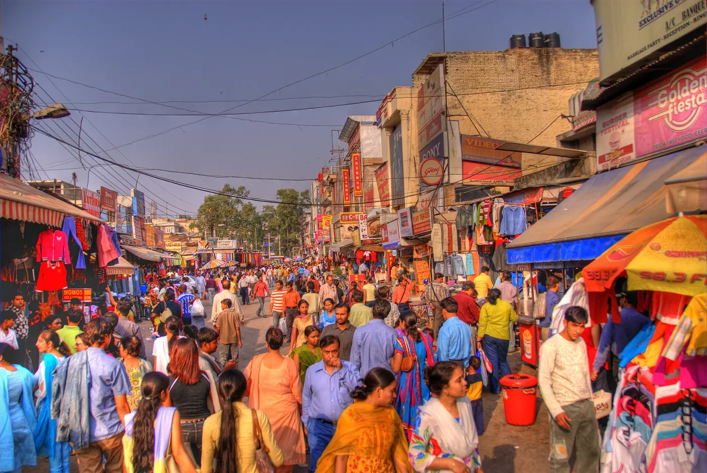 Dense crowds of shoppers moving through Lajpat Nagar Central Market's main lane, lined with clothing stalls and shop signage
