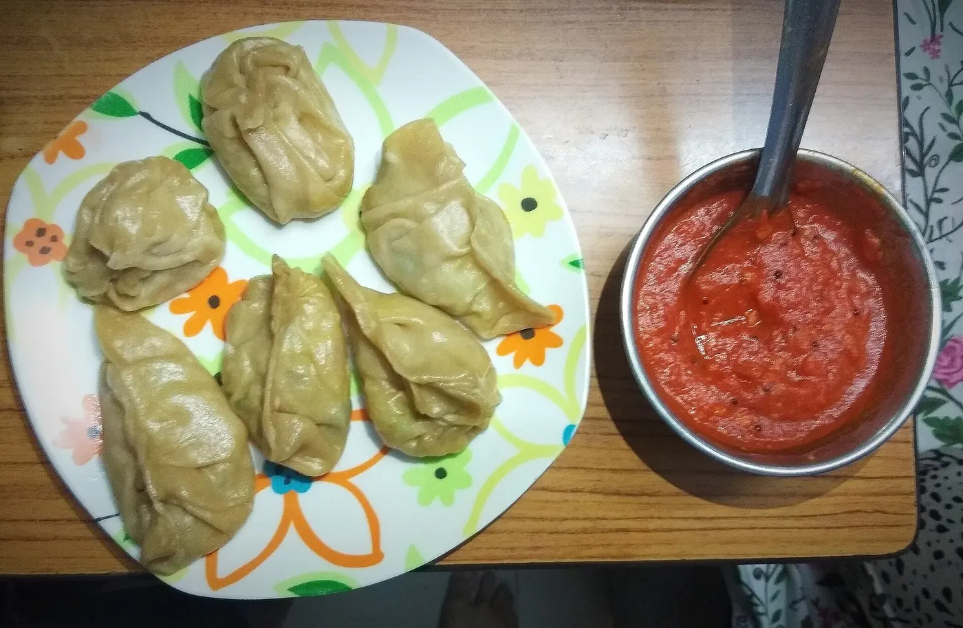 A plate of steamed momos served with a bowl of spicy red chilli chutney, the neighbourhood's signature dish