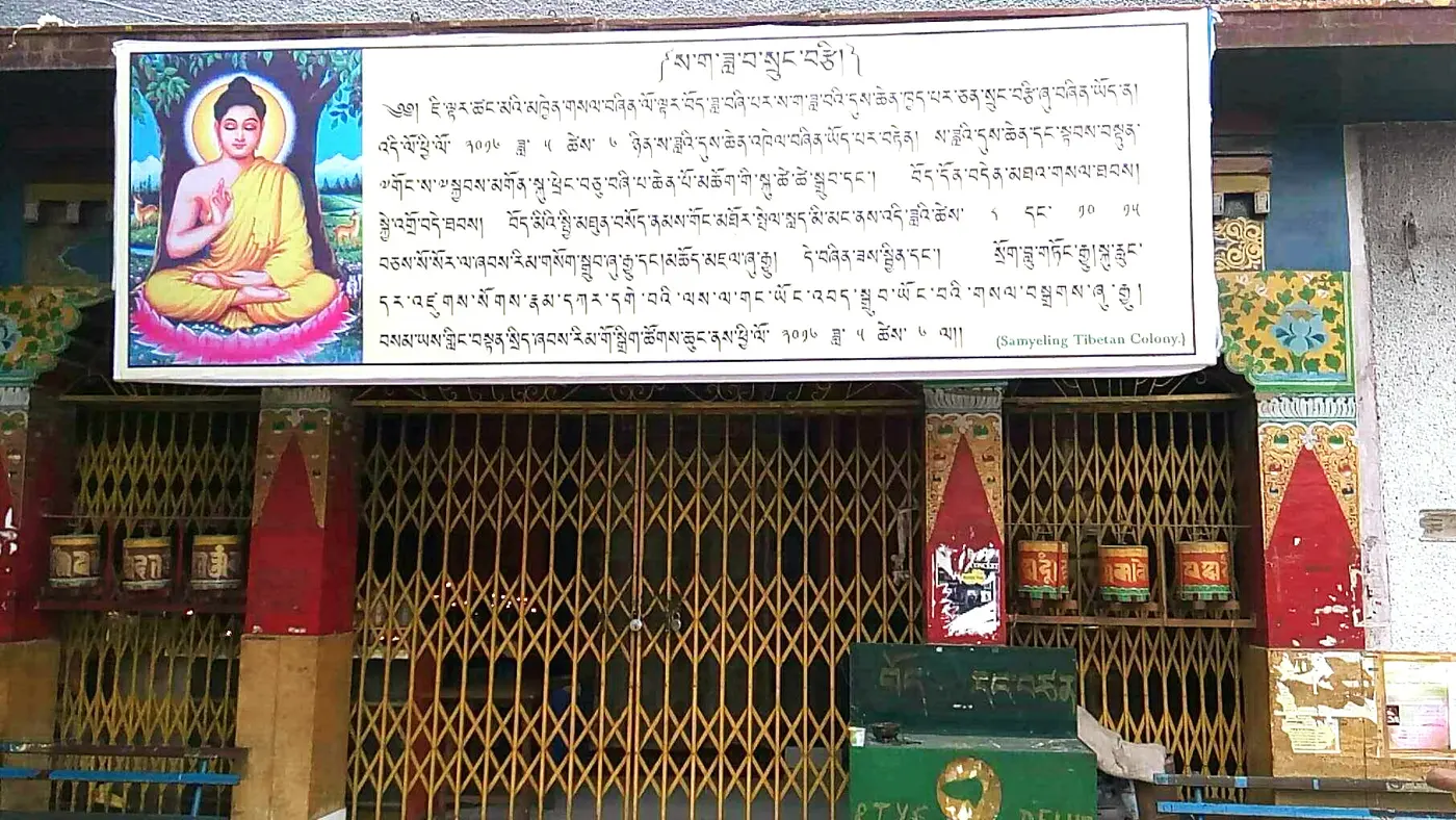The painted entrance of a Tibetan Buddhist monastery in Majnu Ka Tilla, with a Buddha mural, prayer wheels, and Tibetan script banners