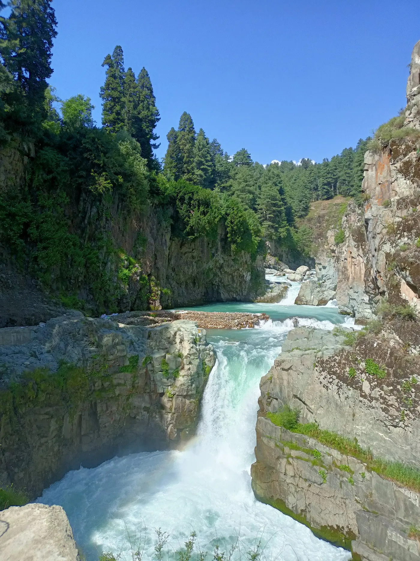 Wide-angle view of Aharbal Falls crashing through a rocky gorge from the main viewpoint, with safety railings in the foreground