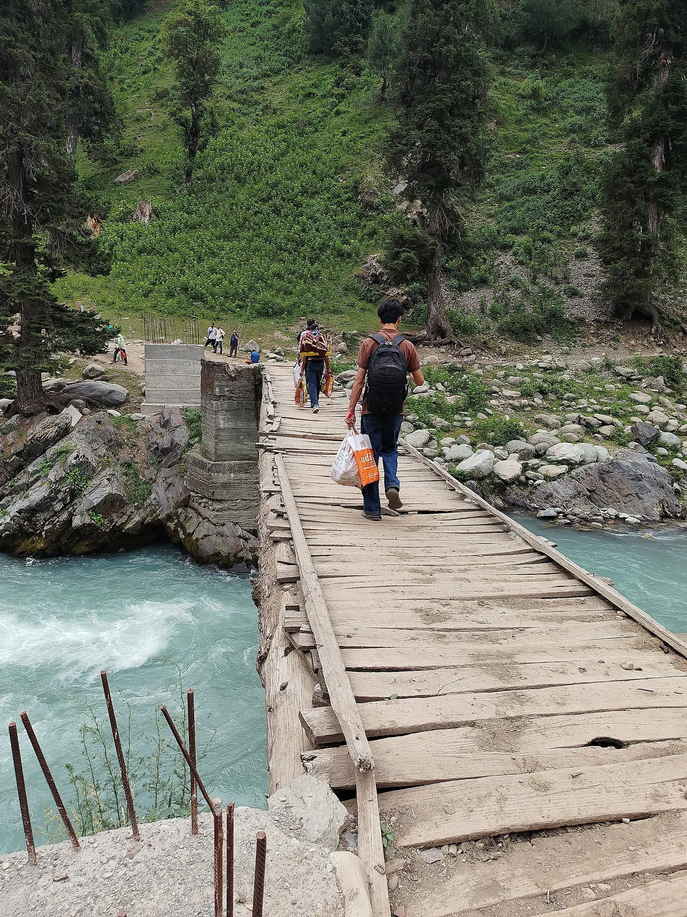 Trekkers crossing a wooden footbridge over the Veshaw River on the trail toward Kongwattan meadow, en route to Kounsarnag Lake