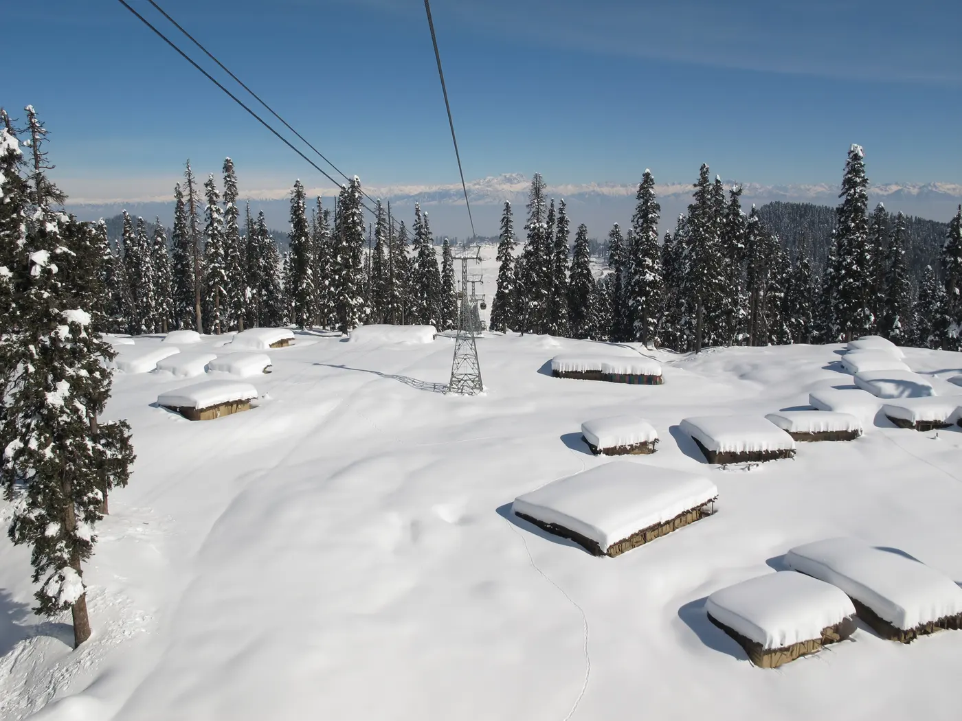 Gulmarg Gondola cable car tower rising above snow-covered huts near Apharwat Peak