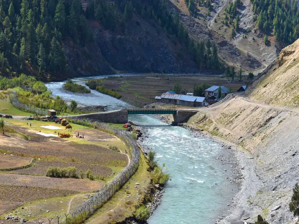 A bridge over the Kishanganga River amid farm fields and a small settlement in the remote Tulail Valley beyond Dawar