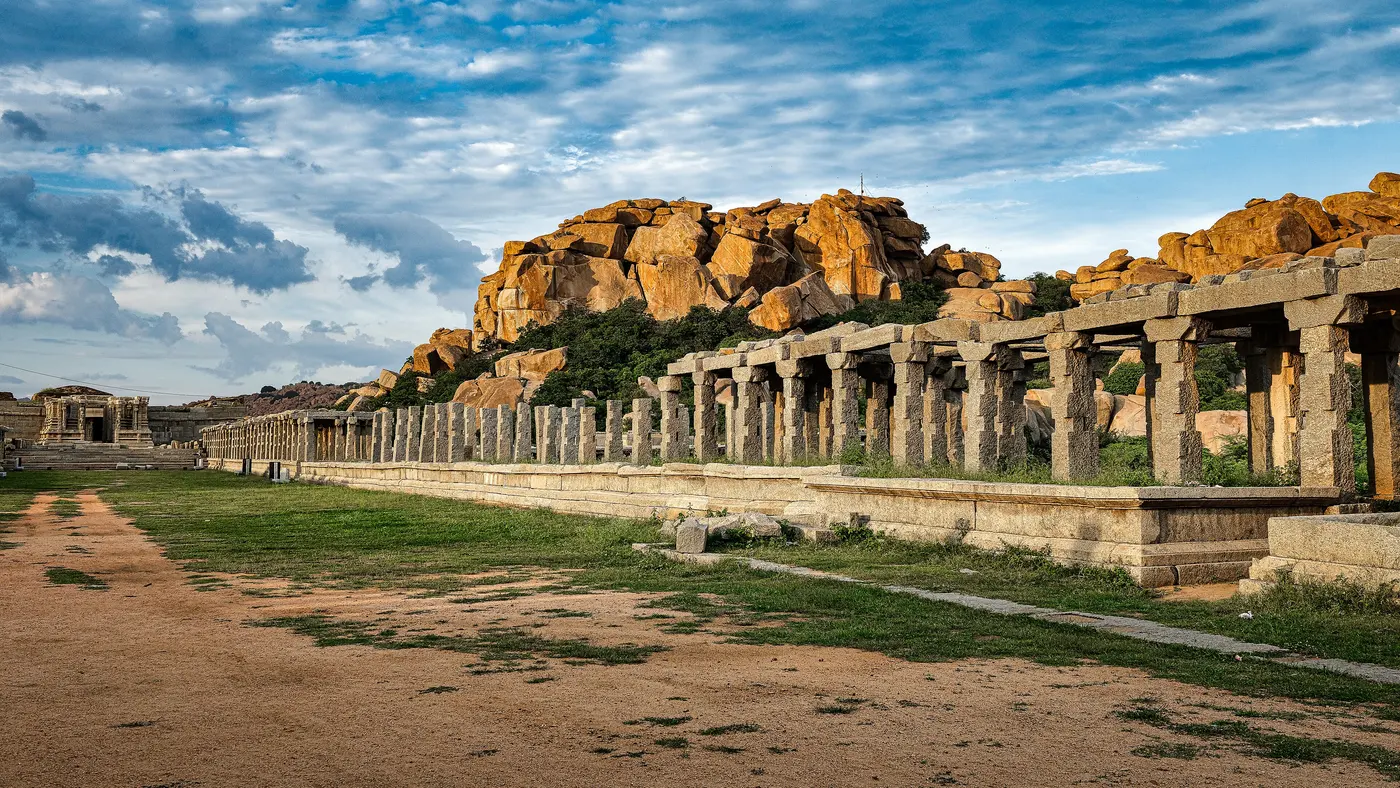 The surviving stone colonnade of the ancient Hampi Bazaar market street, boulders rising behind