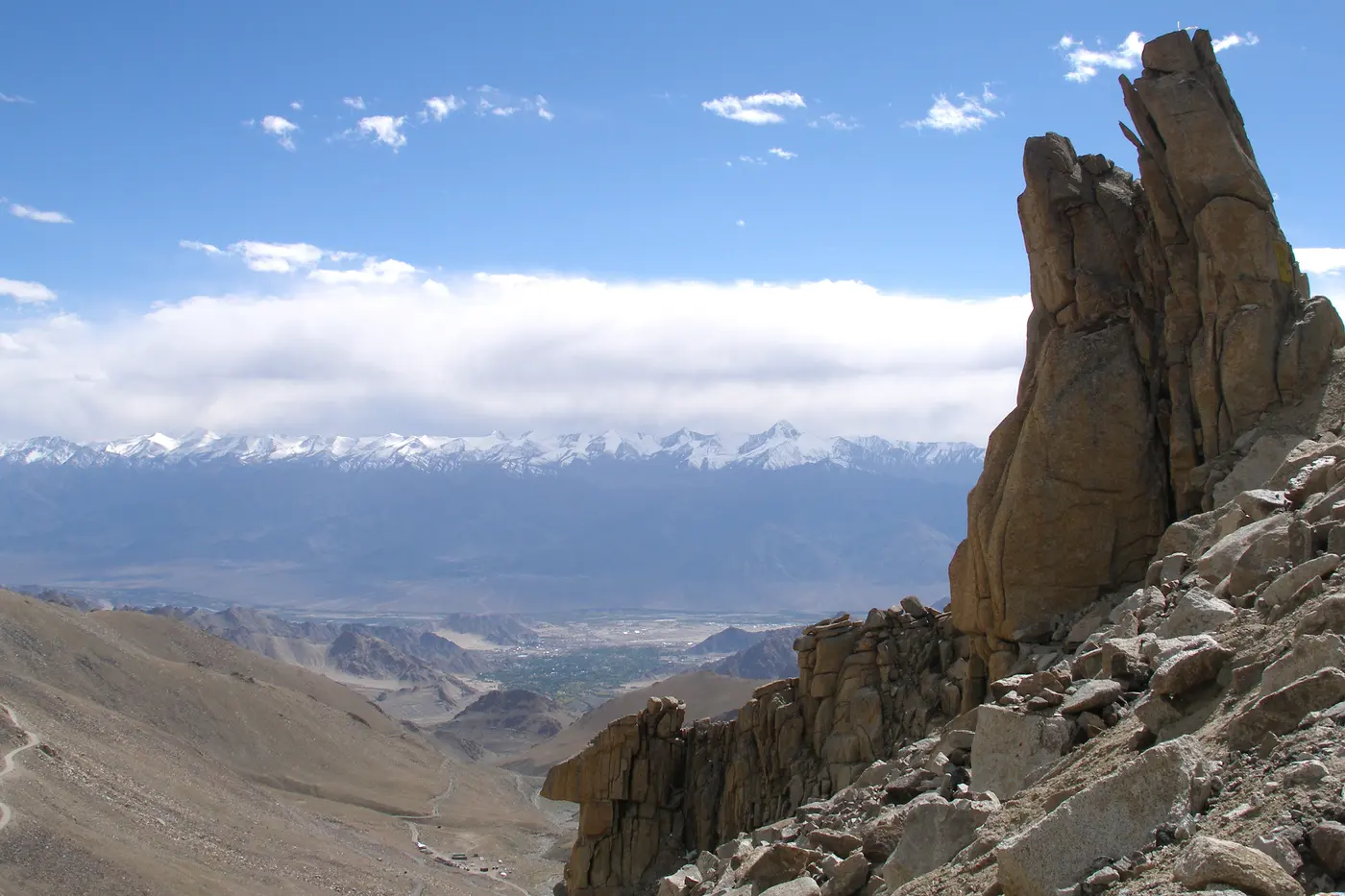 Rocky outcrop near the Khardung La summit overlooking the Indus valley and Leh town, with snow-capped peaks beyond