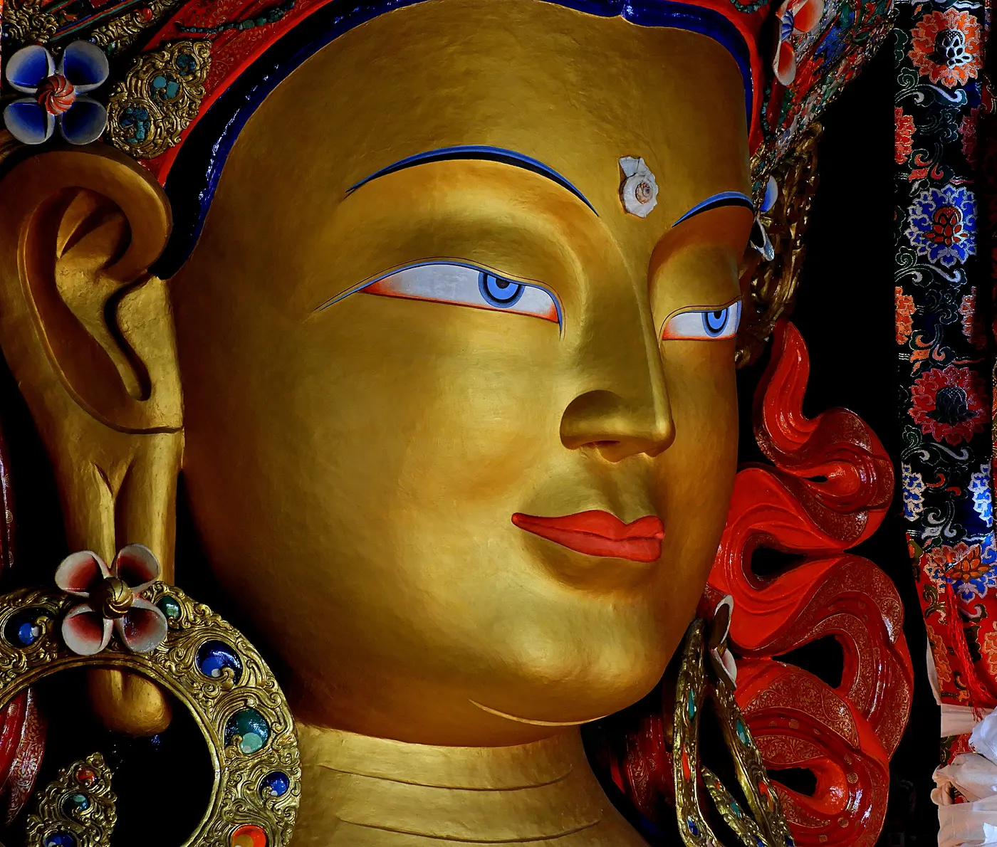 Close-up of the gilded, serene face of the 15-metre seated Maitreya Buddha statue inside Thiksey Monastery