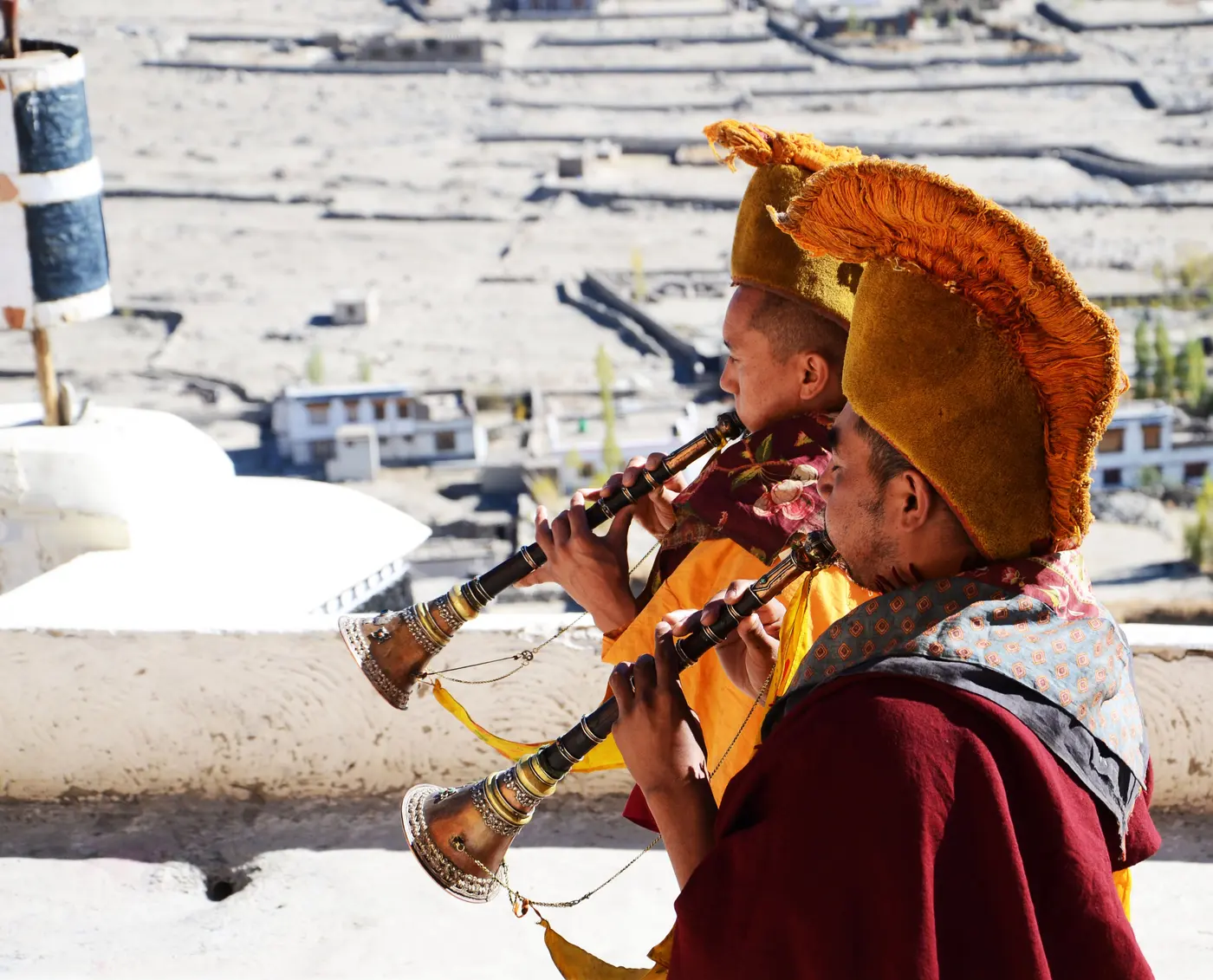 Thiksey monks in ceremonial hats playing long horns on the monastery rooftop overlooking the Indus valley
