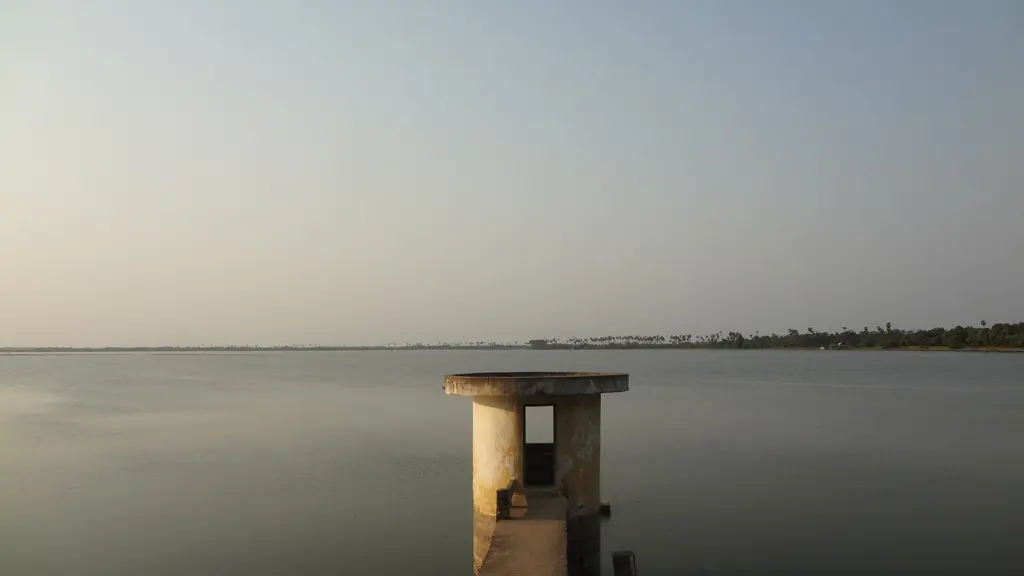 Bahour Lake's still waters with a stone sluice structure and distant palm-lined shore