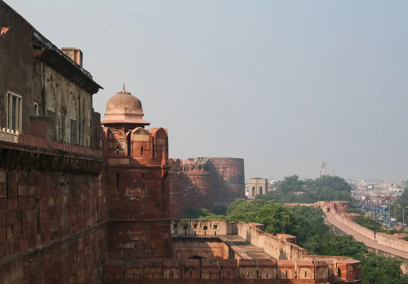 Red-sandstone domed tower and battlements of Agra Fort, with the fort's inner walls stretching toward the city skyline