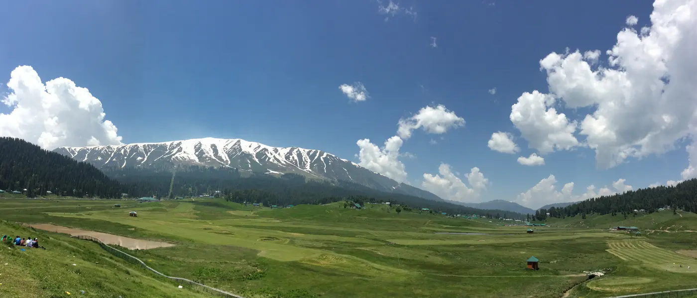 Gulmarg's green summer meadow, home to the world's highest golf course, with snow-capped Pir Panjal peaks behind