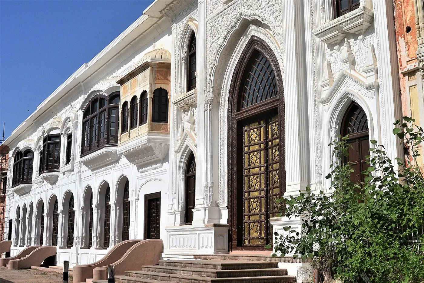 Restored white facade of Mubarak Mandi Palace with ornate arched windows and a gilded doorway in Jammu's old city