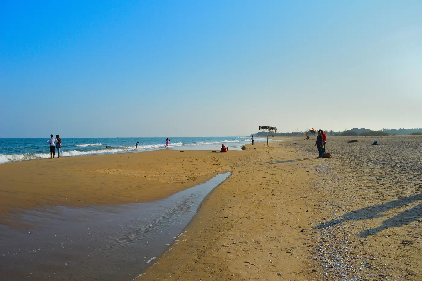 Visitors walking the quiet sandy shore of Paradise Beach near Chunnambar, Puducherry